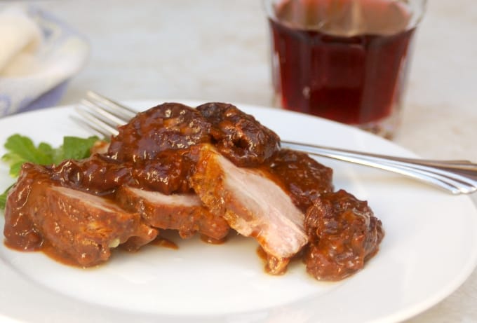 Sliced slow cooker pork roast with prunes on white dinner plate with fork.