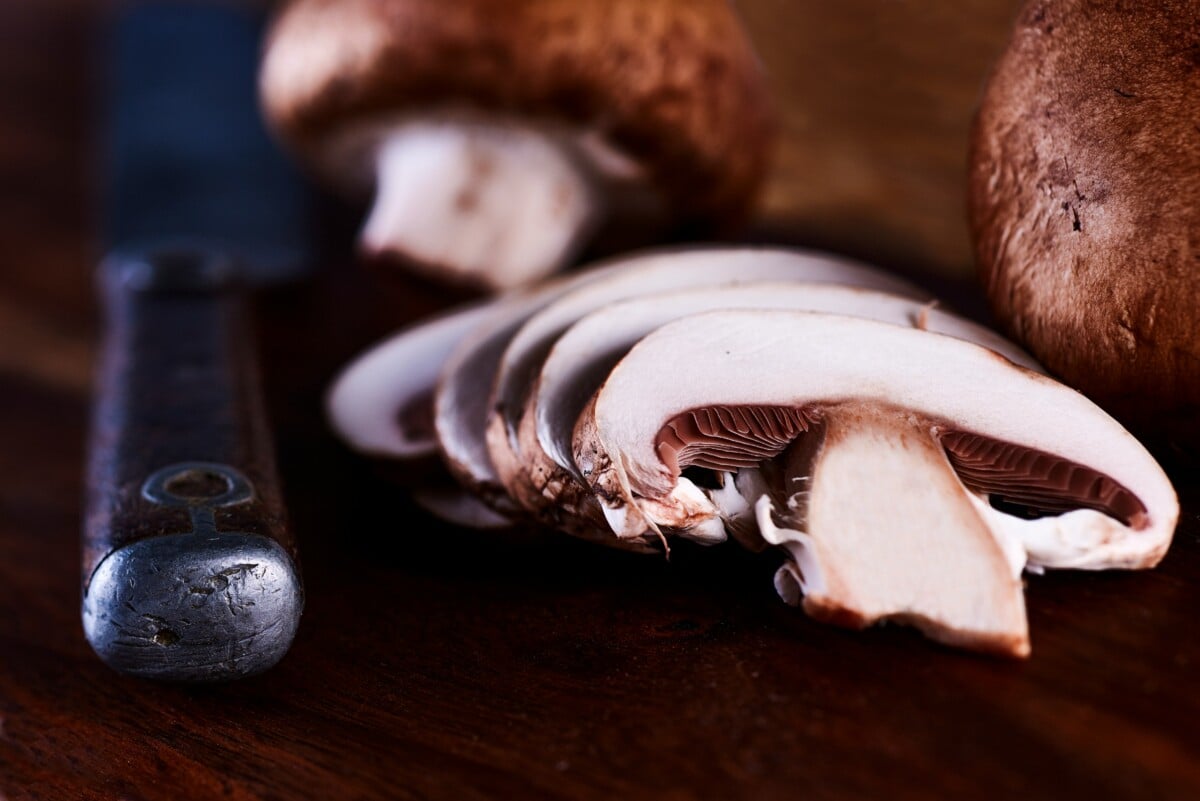 close up of sliced brown mushroom on wooden board with knife alongside