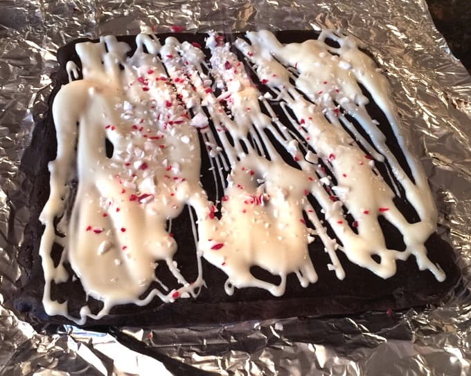 Fresh baked Peppermint Chocolate Cookie Bars drizzled with icing and crushed candy canes sitting on tin foil