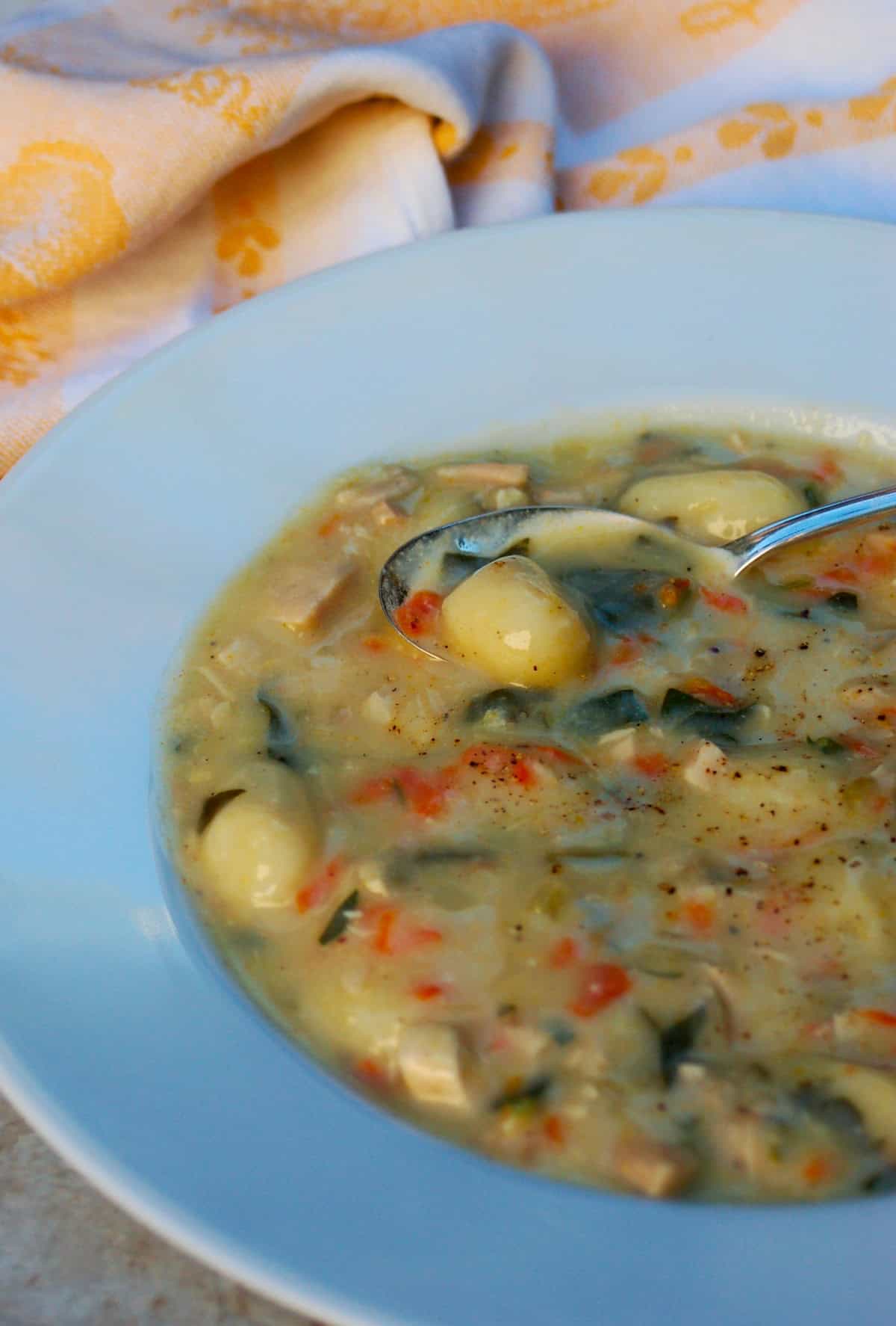 Chicken Gnocchi Soup in white bowl with spoon and cloth napkin.