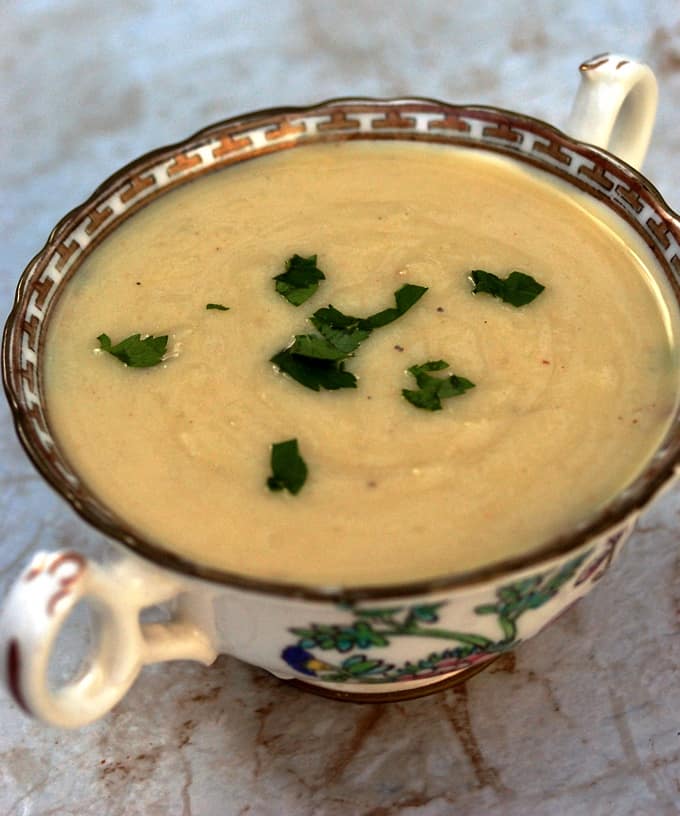 Small china bowl with potato artichoke soup garnished with chopped parsley