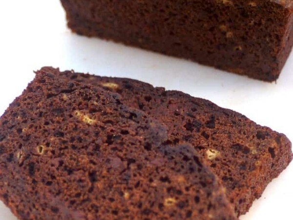 loaf of chocolate banana bread on white cutting board with 2 slices in foreground