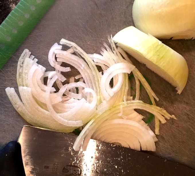 Onions cut in half moons on cutting mat with knife