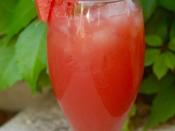 Watermelon Agua Fresca in tall glass with watermelon wedge behind green plant