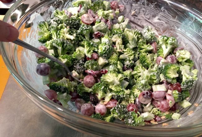 Tossing together broccoli salad ingredients and dressing in a bowl