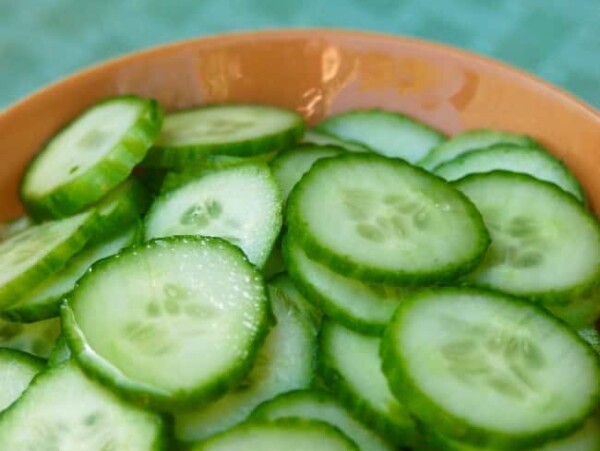 slices of english cucumber in a wooden bowl on aqua background