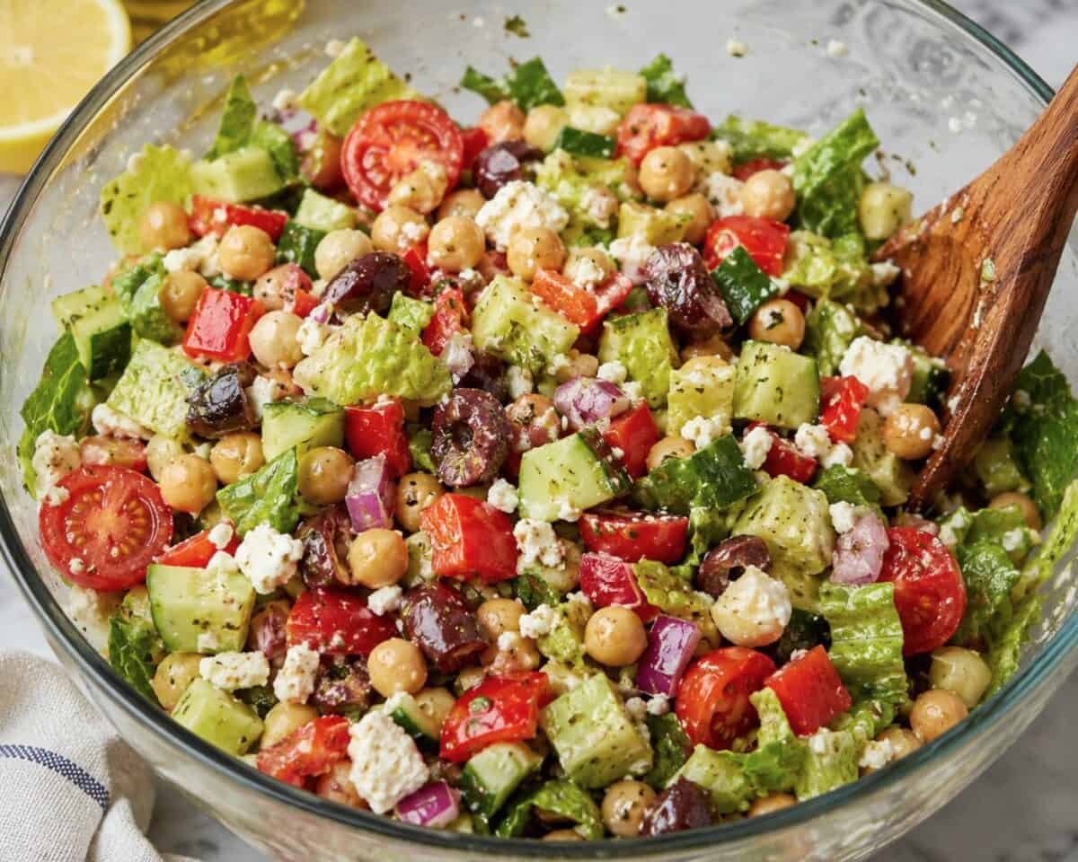 Tossing Chopped Greek Salad in glass bowl.