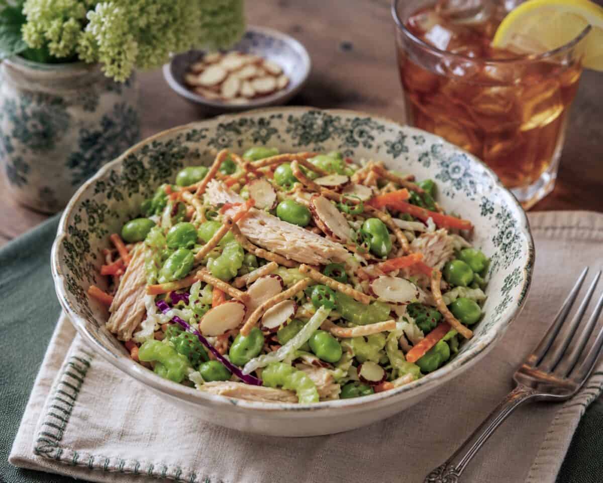 Crunchy Asian chicken salad in a vintage bowl with fork and linen napkin and glass of iced tea in the background.