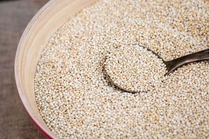 Organic uncooked quinoa grain in wooden bowl.
