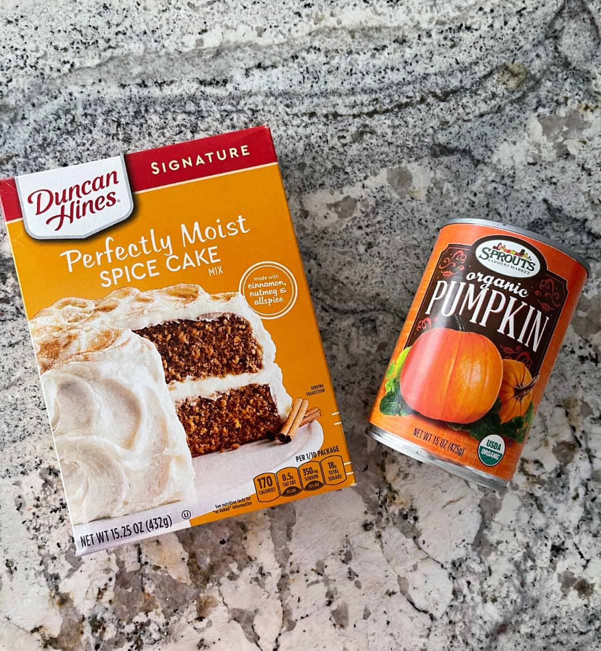 Ingredients including box of Duncan Hines spice cake mix and can of organic pumpkin puree on granite.