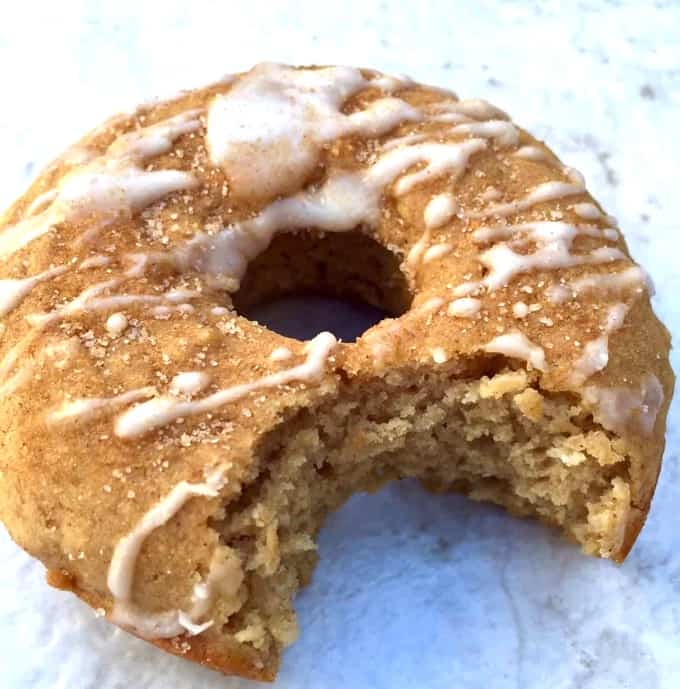 Baked apple cinnamon doughnut with icing on napkin with bite taken out of it.
