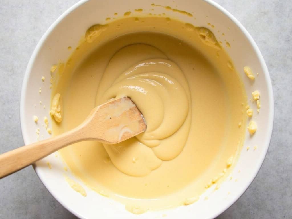 Mixing bowl stirring batter with wooden spoon shot from above.