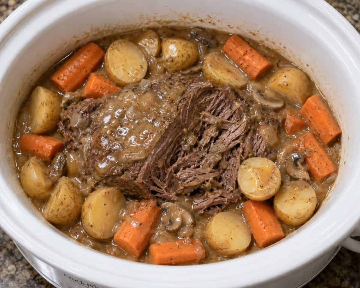 Slow cooker pot roast with potatoes and carrots in a white slow cooker.