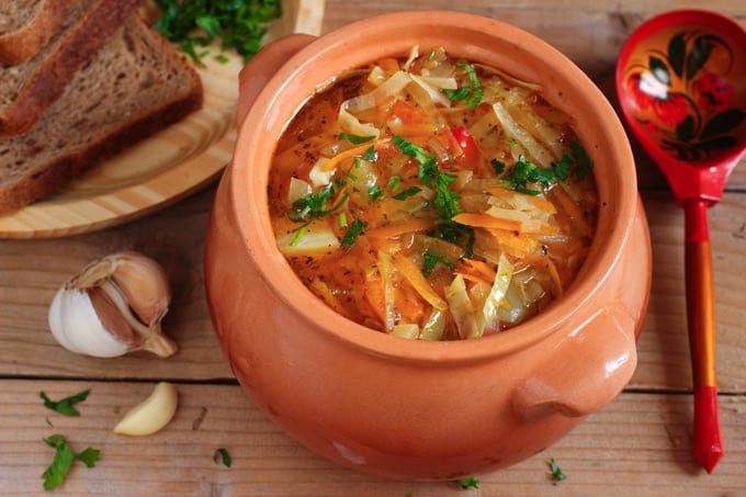Vegetarian Cabbage Soup in a soup crock with spoon on a wooden table