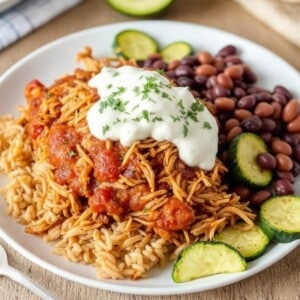 white plate filled with salsa chicken, beans, zucchini, garnished with sour cream and cilantro