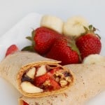 peanut butter strawberry flatout wrap halves crossed on a plate with strawberry banana garnish