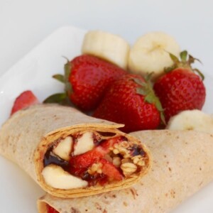 peanut butter strawberry flatout wrap halves crossed on a plate with strawberry banana garnish