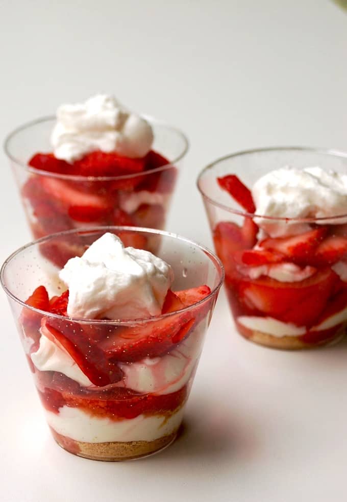 3 small dessert glasses with no-bake strawberry cheesecake parfaits topped with whipped cream