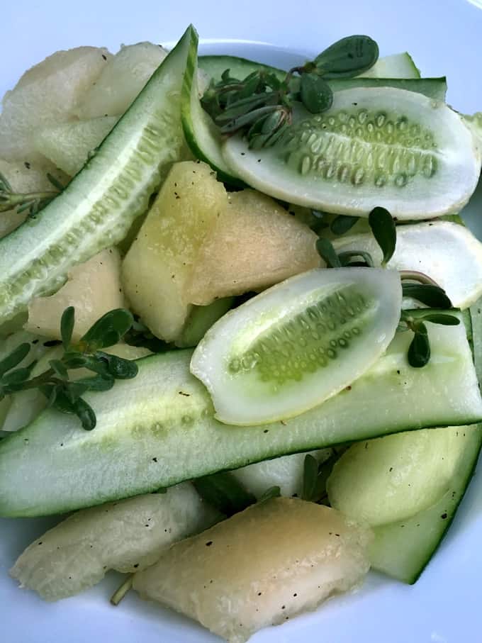 Simple melon cucumber salad with fresh herbs on white plate.