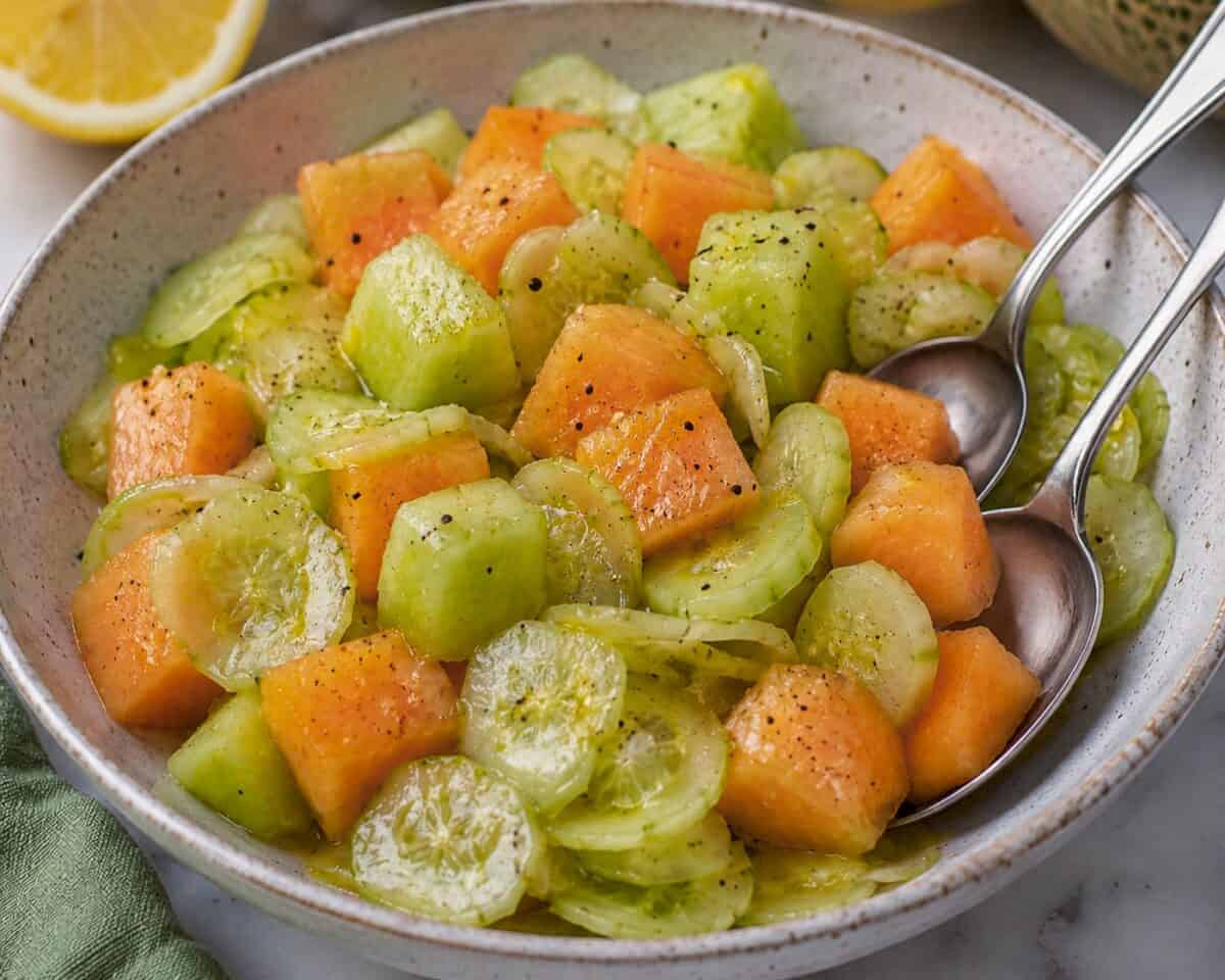 Melon Cucumber Salad with chopped honeydew, cantaloupe and thinly sliced cucumber in a ceramic bowl with serving spoons.