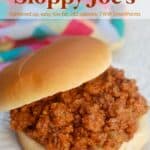 Sloppy Joe on hamburger bun on white plate with colorful napkin in the background.