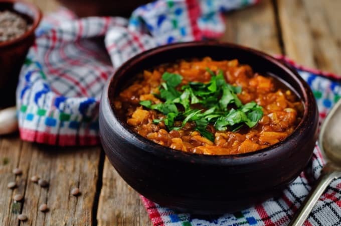 Lentil stew in a brown bowl on a wood background with colorful dish towel