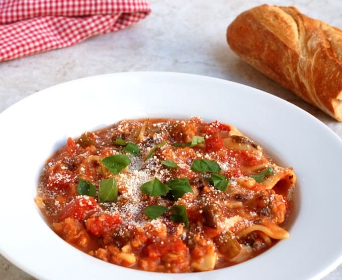 Lasagna soup topped with grated cheese and herbs in white bowl with fresh bread on the side.