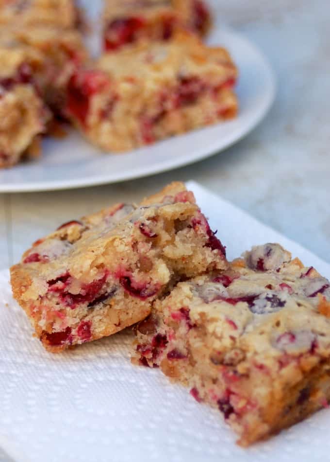Low fat cranberry bars on white napkin with plate of cranberry bars in the background.