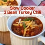 Slow cooker 3-bean turkey sausage chili in white mug topped with shredded cheese.
