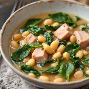 italian pork and white bean stew with spinach in pottery bowl with spoon alongside