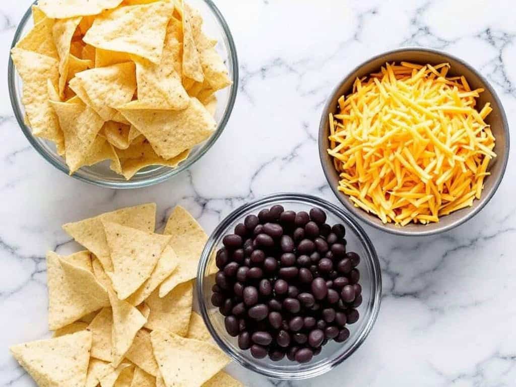 marble counter with bowls of tortilla chips, shredded cheese and black beans shot from above