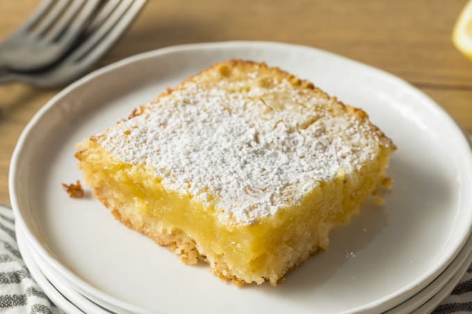 Homemade Low-Fat Lemon Bar for dessert on a stack if white plates topped with powdered sugar