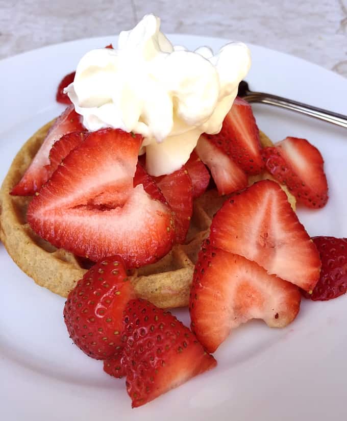Toasted waffle topped with sliced strawberries and whipped cream.