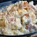 Creamy red, white and blue potato salad sprinkled with paprika in blue ceramic bowl.