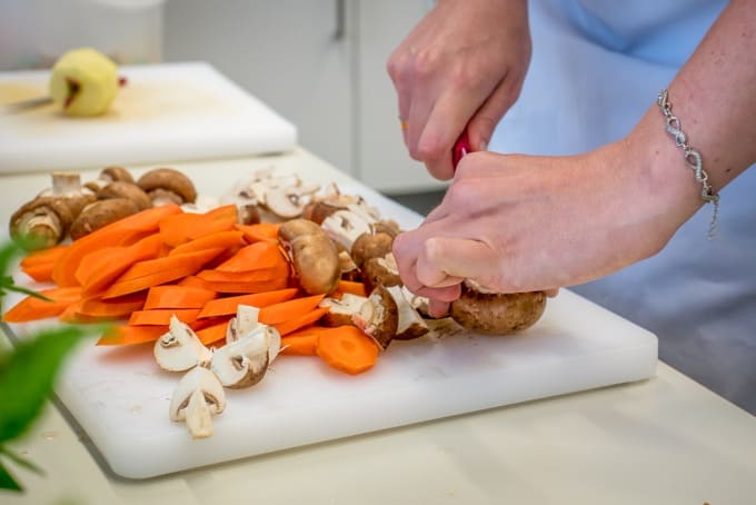 Female hands chopping carrots and mushrooms on white cutting board