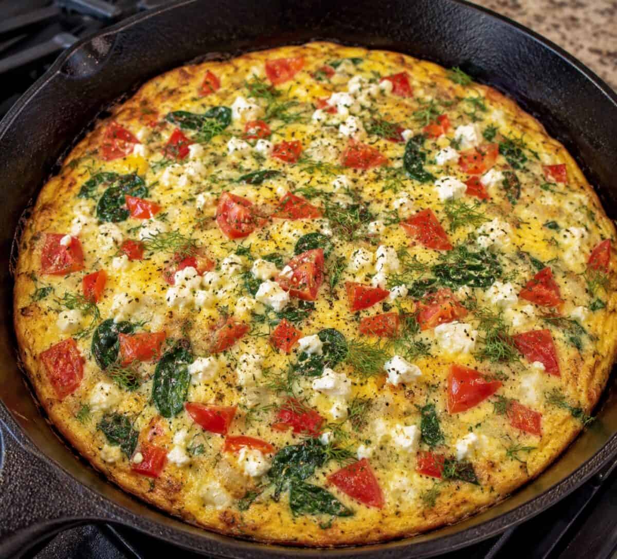 Fresh cooked Greek Frittata in cast iron skillet topped with fresh chopped dill.