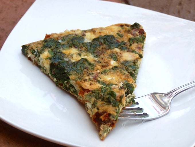 Piece of Greek frittata with spinach and feta on white plate with fork.