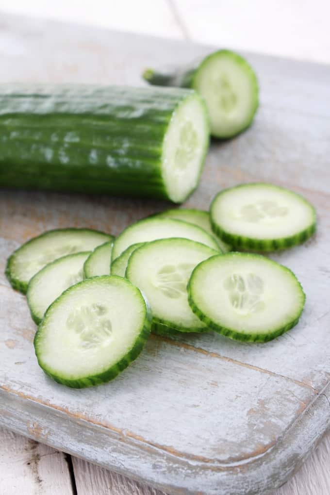 Fresh cucumber slices on white-washed cutting board.