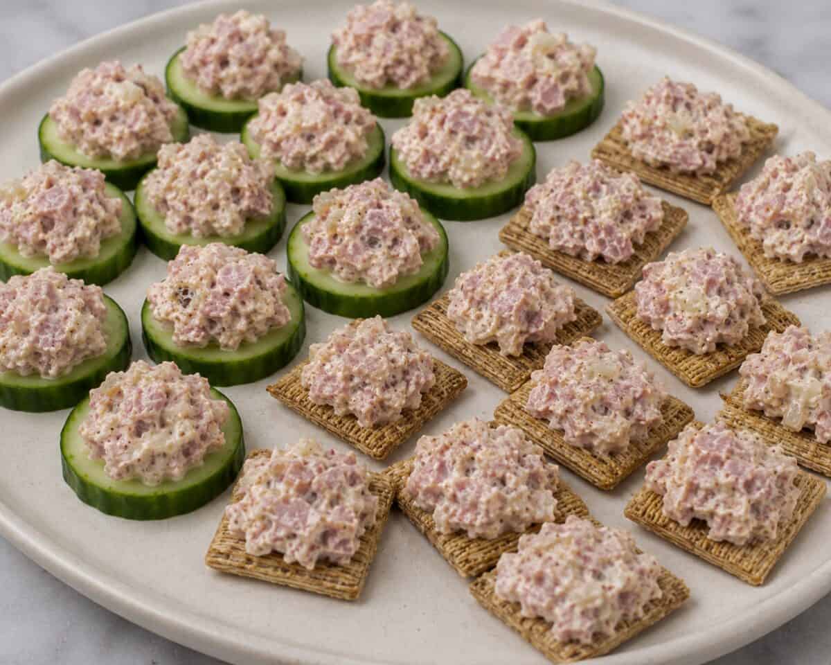 Ham Salad Spread on cucumber slices and Triscuit crackers on white serving platter.