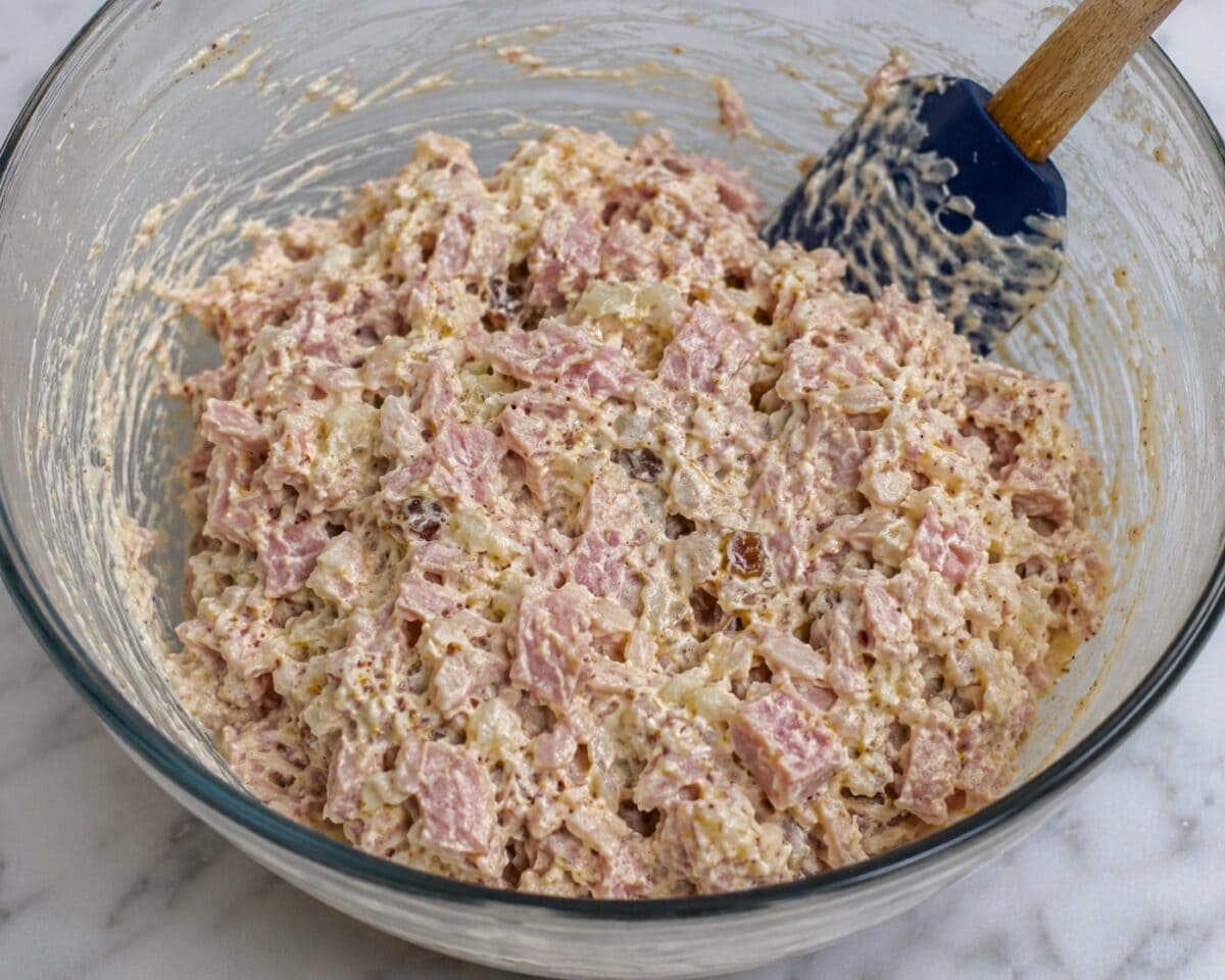 Combining ham salad spread in a glass bowl with a rubber spatula.