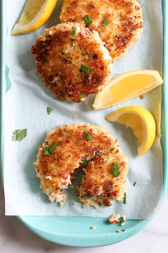 3 shrimp cakes decoratively arranged on oblong plate sprinkled with parsley and garnished with lemon wedges