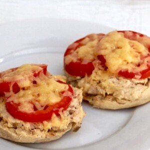 two english muffin halves topped with tuna salad, sliced tomato and melted cheese on a white plate