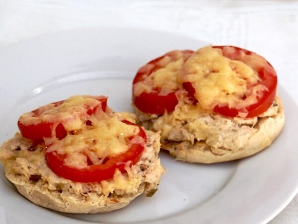 two english muffin halves topped with tuna salad, sliced tomato and melted cheese on a white plate