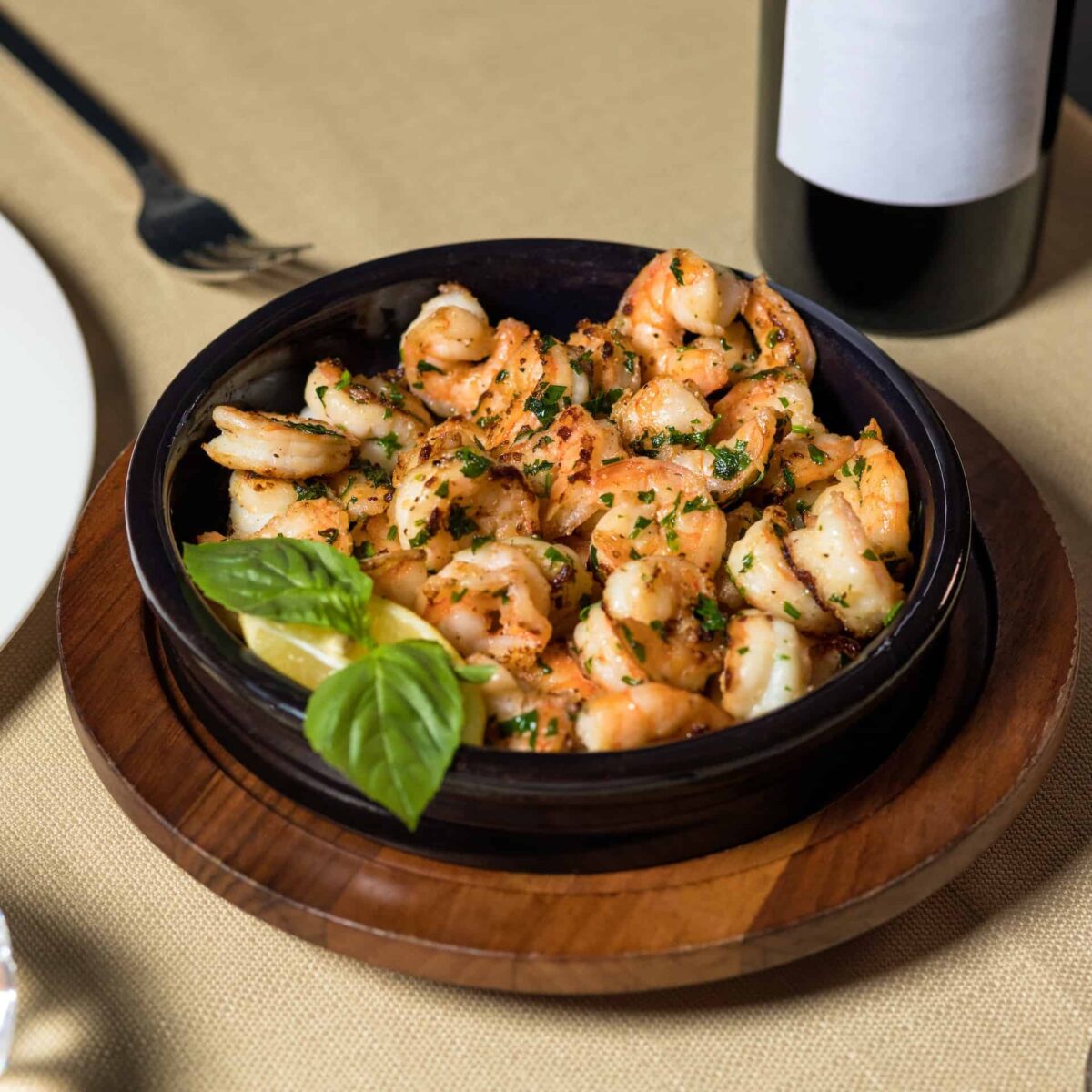 garlic shrimp garnished with basil on a wooden platter with bottle of wine in the background