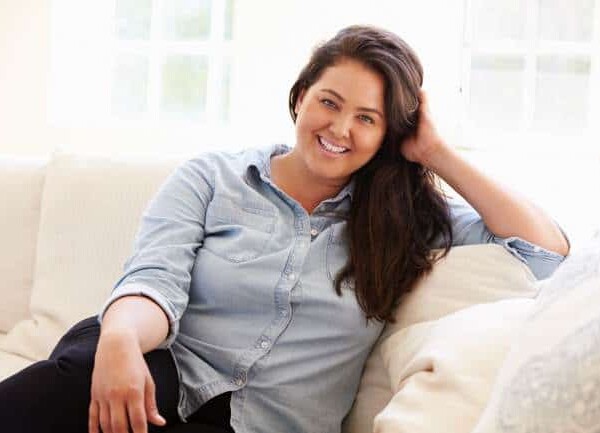 Pretty woman with long dark hair wearing light blue blouse sitting on sofa