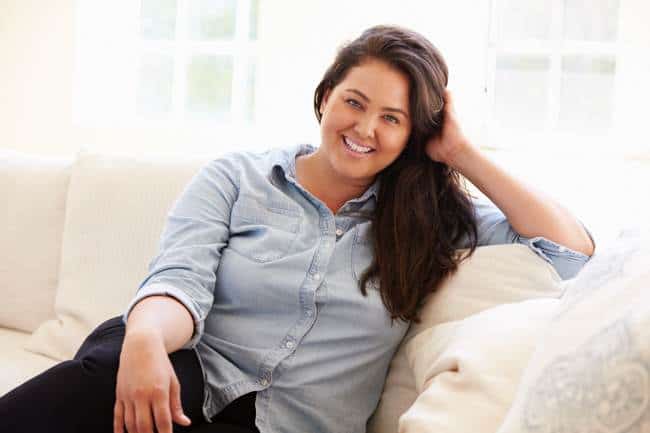 Pretty woman with long dark hair wearing light blue blouse sitting on sofa