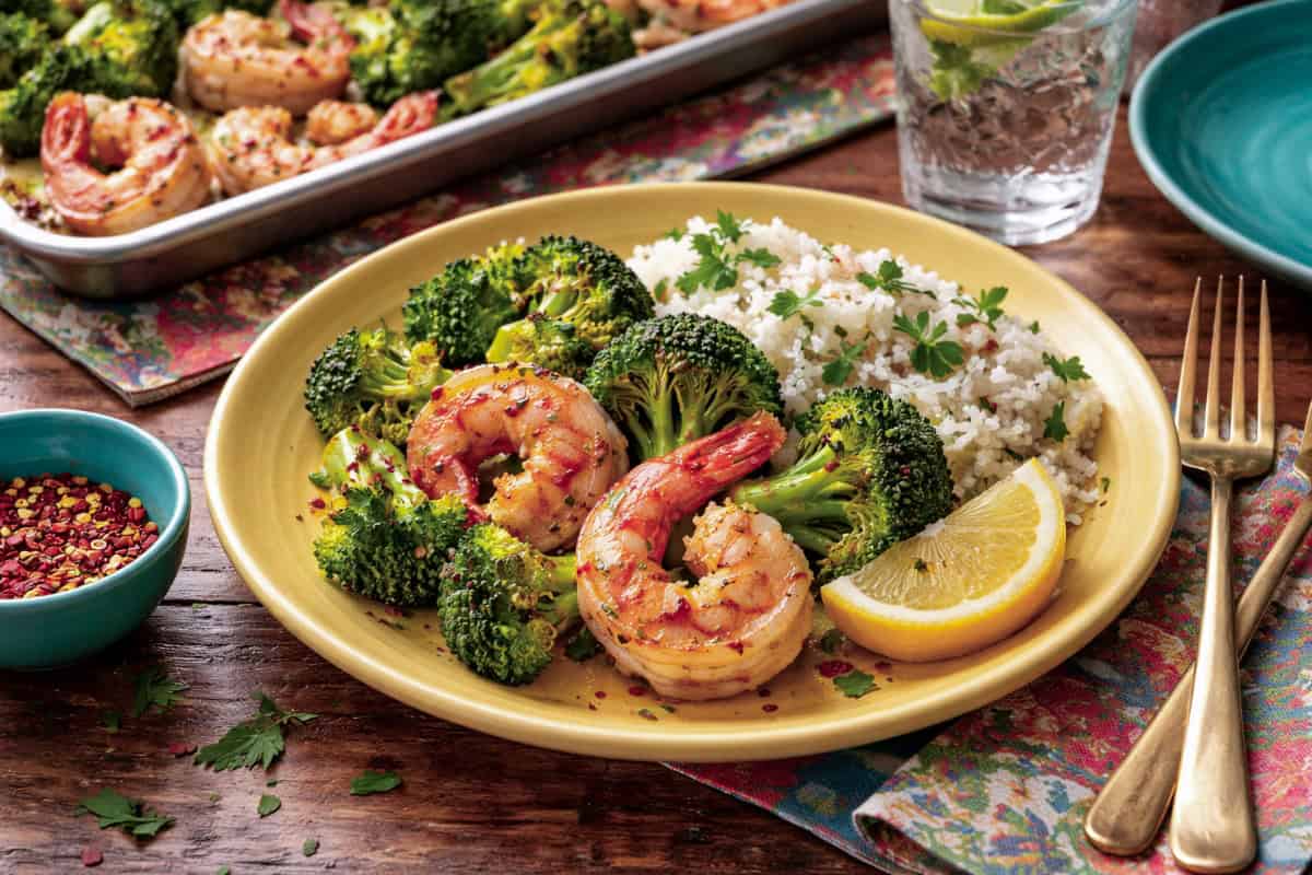 Sheet Pan Roasted Shrimp and Broccoli on a yellow plate with lemon wedge and couscous.