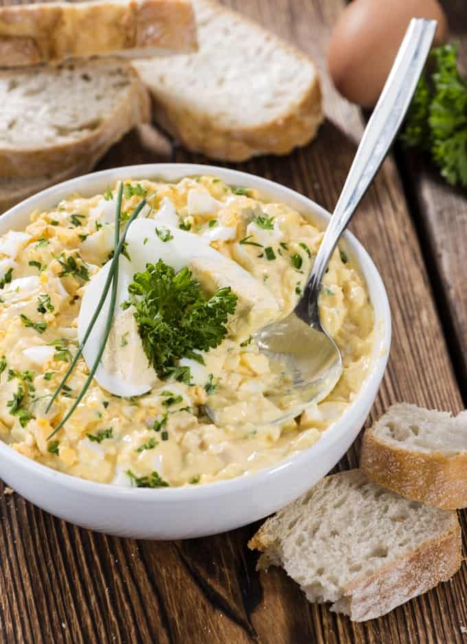 Bowl with Egg Salad and slices of bread on dark wooden background