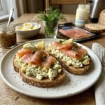Open Face Egg Salad Toasts topped with smoked salmon and dill with hard boiled eggs, mustard, whole grain bread in background