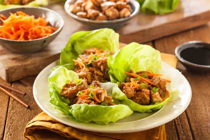Asian Lettuce Wraps on white plate with shredded carrots and soy sauce in background.